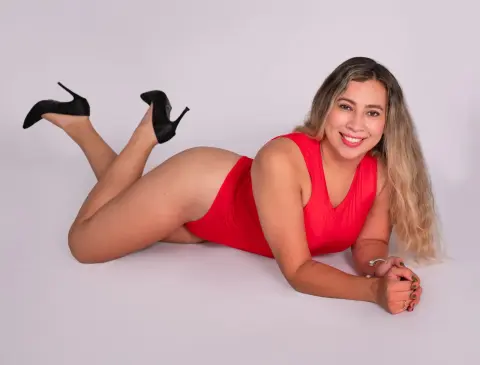 Smiling woman in a red bodysuit and black high heels lying on a white background.