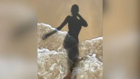 Shadow of a woman standing in ocean waves on a sunny beach during a peaceful summer day.