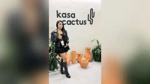 Smiling woman in a black leather jacket and mini skirt holding a wine bottle at Kasa Cactus decor setting.