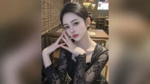 AgelaHui poses in a black lace long-sleeve top with her hands framing her face, showing her dark hair pulled back in a bun.