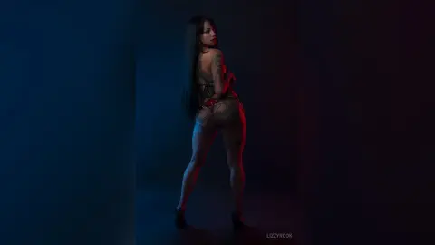 Tattooed woman in a black lace bodysuit posing in moody blue and red studio lighting.