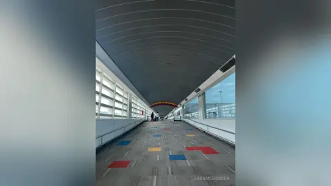 Modern airport walkway with large windows and colorful floor patterns under a curved ceiling.