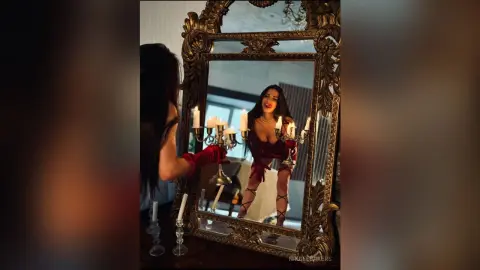 Smiling woman in a red velvet outfit reflected in an ornate vintage gold mirror surrounded by glowing candles.