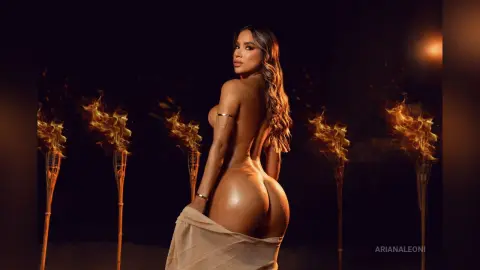 Glamorous woman in a nude bikini posing amidst glowing torches in a dark, moody setting.