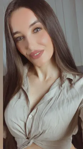 Smiling woman with long brown hair wearing a beige linen button-down shirt in a bright indoor setting.