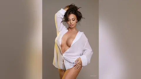 Glamorous woman in an open white button-down shirt posing in a studio with warm lighting.