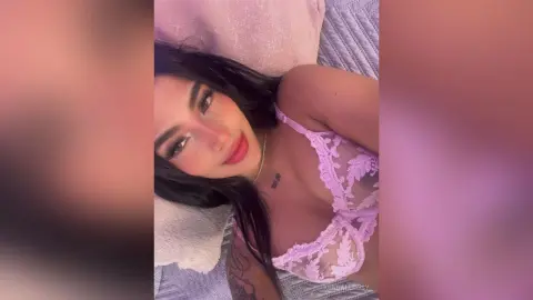 KendallRosy smiles while lying on a bed wearing a light purple lace bra.