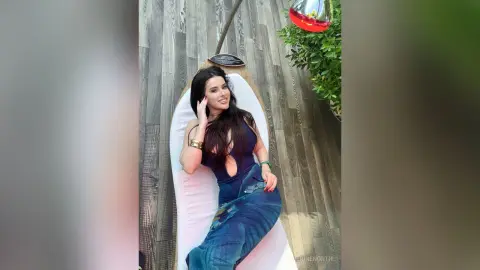 Smiling woman in a dark blue bodysuit relaxing on a white lounge chair outdoors on a wooden deck.