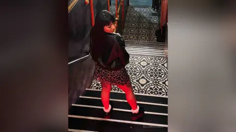 Stylish woman in a black leather jacket and leopard print skirt posing on patterned stairs in a moody setting.