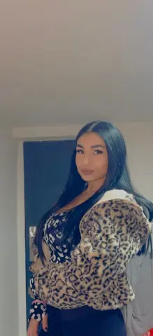 Young woman with long dark hair wearing a leopard print faux fur jacket in a modern indoor setting.