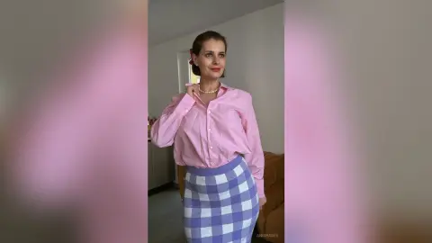 Smiling woman in a pink button-down shirt and blue checkered skirt posing in a bright indoor setting.