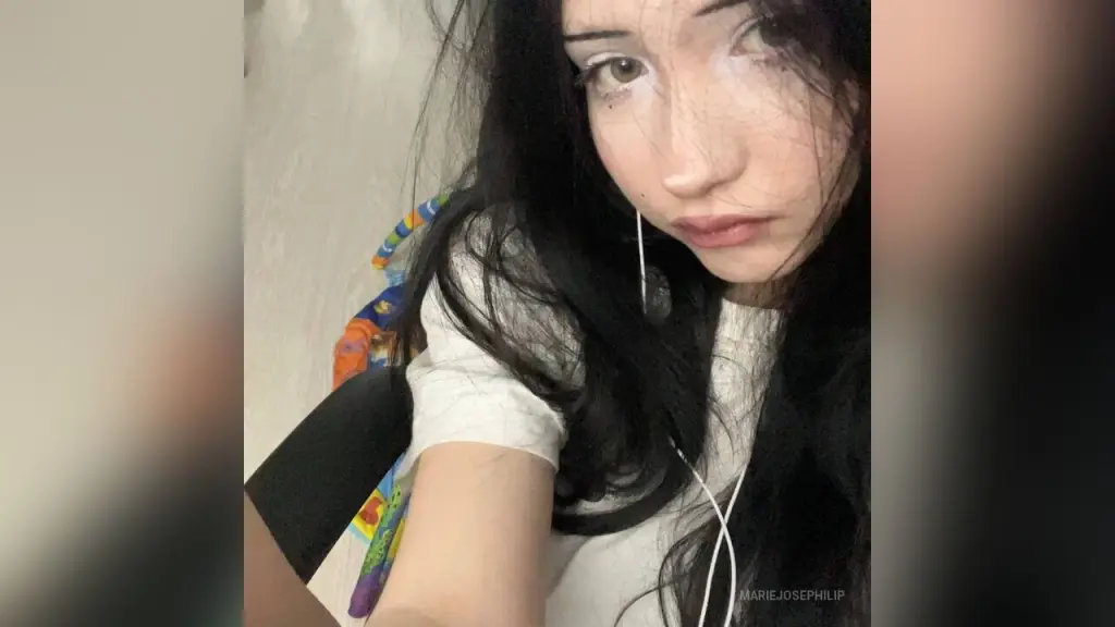 MarieJosePhilip β MarieJosePhilip poses with long black hair and white wired earphones, wearing a simple white t-shirt against a plain light background.