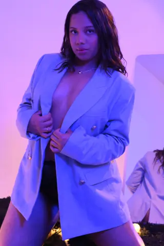 Young woman in an oversized light blue blazer posing in moody purple studio lighting.