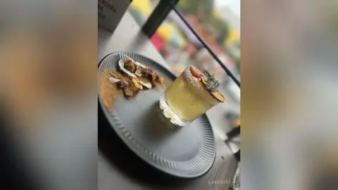 KimRoberth enjoys a refreshing yellow cocktail and a plate of snacks at an outdoor cafe table.