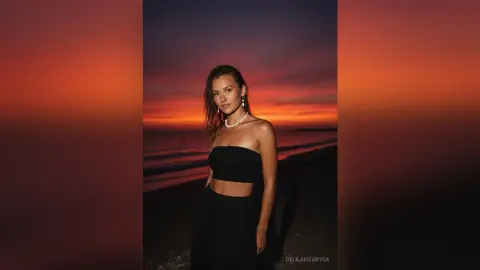 Young woman in a black strapless outfit posing on a beach during a moody sunset.