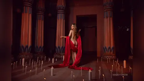 Glamorous woman in a flowing red silk gown standing in a mystical ancient temple lit by glowing candles.