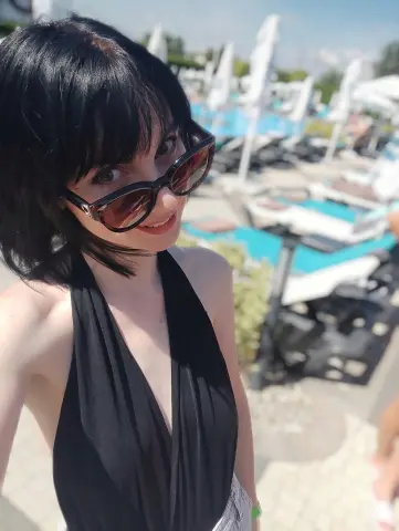 Smiling woman in a black halter neck top wearing sunglasses at a sunny outdoor beach resort.