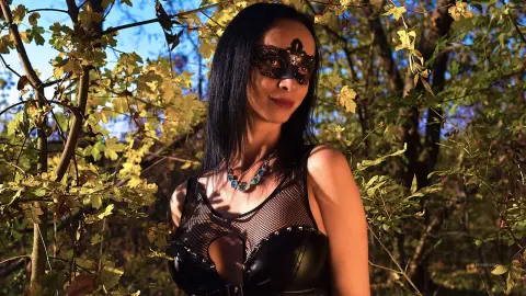 Mysterious woman in a black lace mask and mesh outfit posing in a sunlit autumn forest.