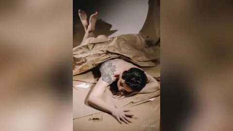 Artistic portrait of a woman lying under brown paper in a moody, minimalist studio setting.