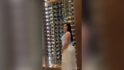 Elegant woman in a light blue top and polka dot skirt standing in a modern luxury wine cellar.