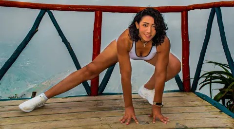 Athletic woman in white sports bra and sneakers stretching on a wooden balcony overlooking a misty mountain view.