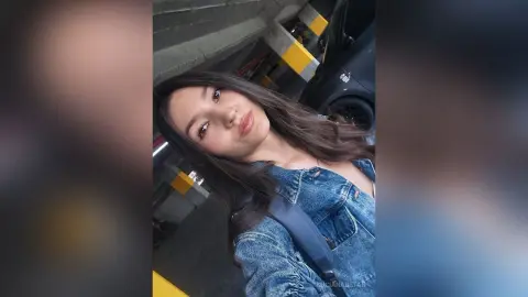 Young woman in a denim jacket smiling in a modern parking garage setting.