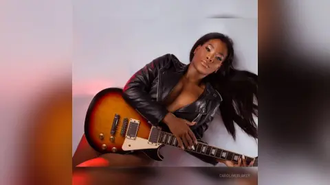 Glamorous woman in a black leather jacket posing with an electric guitar against a soft studio background.