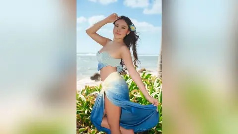 Smiling woman in a blue striped bikini top and ombre sarong relaxing on a sunny tropical beach.