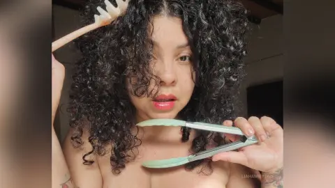 Woman with voluminous curly hair using a hair comb and styling tool in a bright indoor setting.