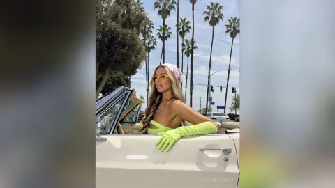 AyshaConnor poses in a white convertible wearing a bright lime green bikini, matching gloves, and yellow sunglasses.