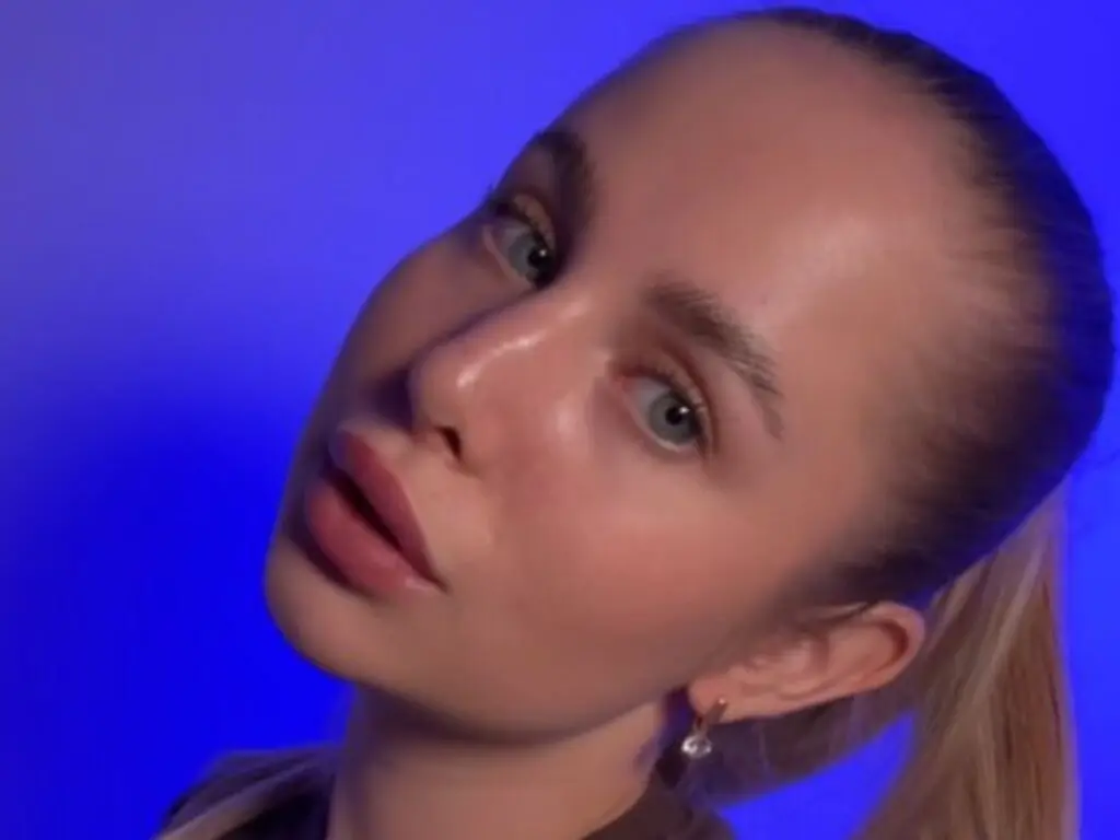 Young woman with blonde hair and natural makeup posing against a vibrant blue background.