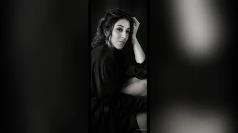 Moody black and white portrait of a woman in a dark shirt posing with a thoughtful expression.