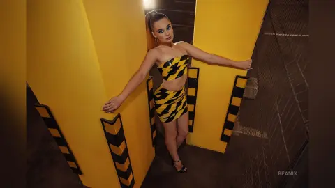 BeaNix stands between yellow walls wearing a yellow and black tiger-print tube dress with her hair in a high ponytail.