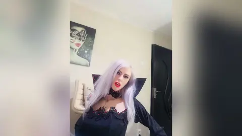 Elegant woman with long silver hair in a black lace outfit posing in a modern minimalist room.