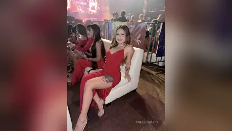 Smiling woman in a red dress sitting on a white sofa at a lively indoor event.