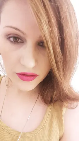 PEARLLxo looks into the camera with long light brown hair and bright pink lipstick, wearing a tan ribbed tank top.
