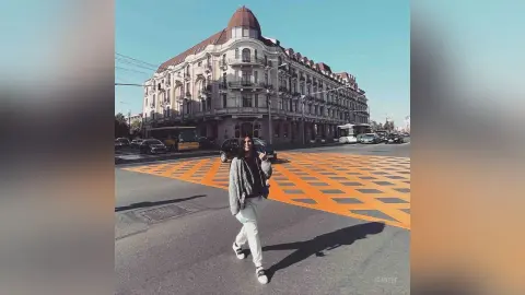 Stylish woman in a grey sweater and white pants walking on a city street near historic European architecture.
