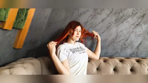 Red-haired woman in a white Dickies t-shirt relaxing on a beige sofa in a modern room.