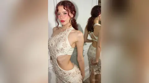Red-haired woman in a white floral cutout cocktail dress posing in a bright indoor setting.