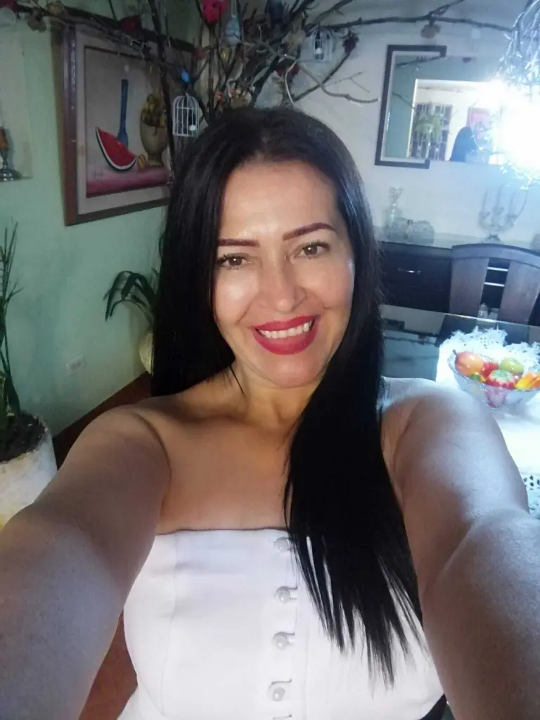 Sarahteikus smiles with her long black hair and bangs, wearing a black sleeveless top while looking directly at the camera.