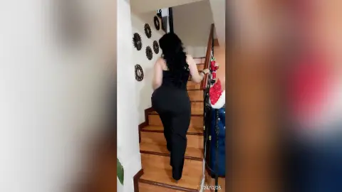 Woman in black jumpsuit walking up wooden stairs in a modern home interior.