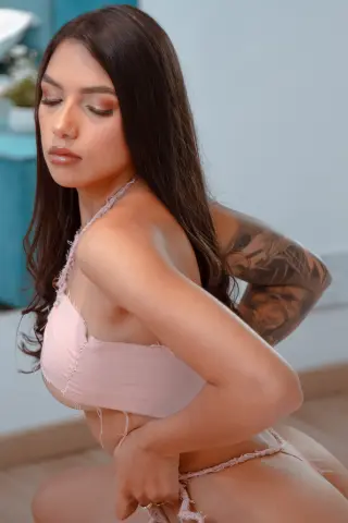 Young woman with long dark hair wearing a pink lace bikini set in a bright, minimalist indoor setting.