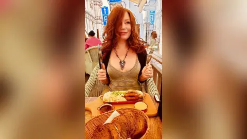Redheaded woman in a lace top enjoying a hearty meal at an outdoor restaurant terrace.