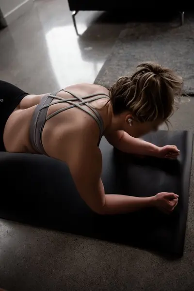 Fit woman in grey sports bra performing floor yoga exercises on a mat in a moody gym setting.