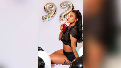 Young woman in a black satin top celebrating a birthday with silver number 92 balloons in a festive mood.
