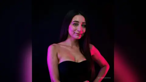 Smiling woman in a black strapless dress posing against a dark background with moody pink lighting.