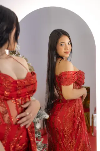 Young woman in a glamorous red sequin evening gown posing in front of a mirror for a festive holiday look.