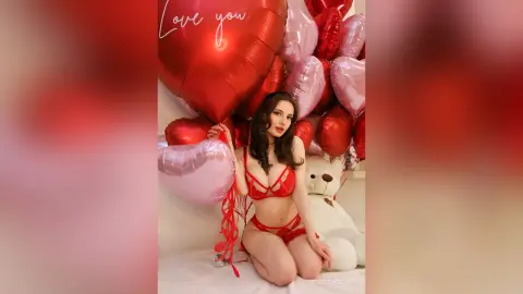 Beautiful woman in red lingerie posing with heart-shaped balloons for a romantic Valentine's Day mood.