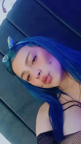 Young woman with vibrant blue hair and natural makeup posing in a cozy indoor setting.