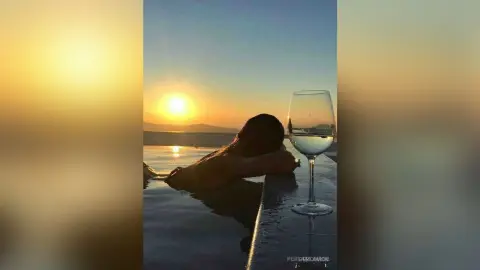 Relaxed woman lounging in an infinity pool at sunset overlooking a calm ocean view.
